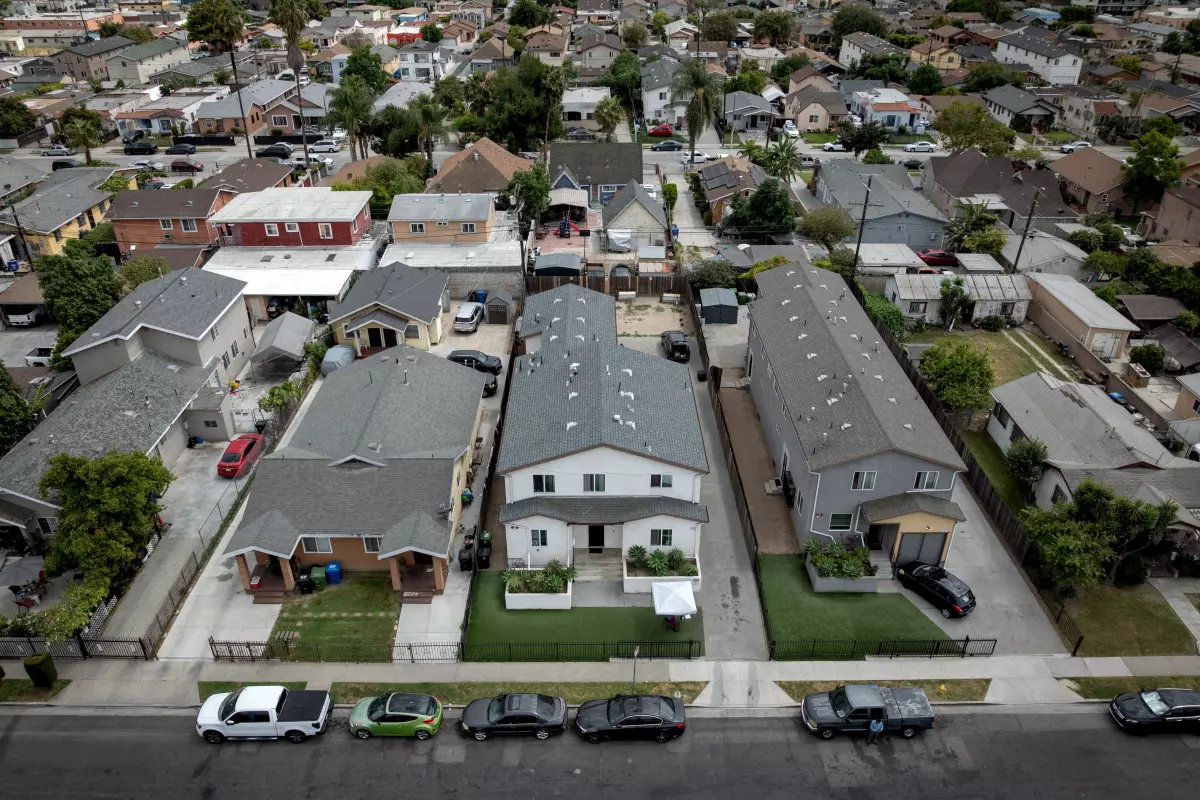 Aerial view of a dense residential neighborhood with closely spaced houses, driveways, parked cars, and narrow yards lining a city street.