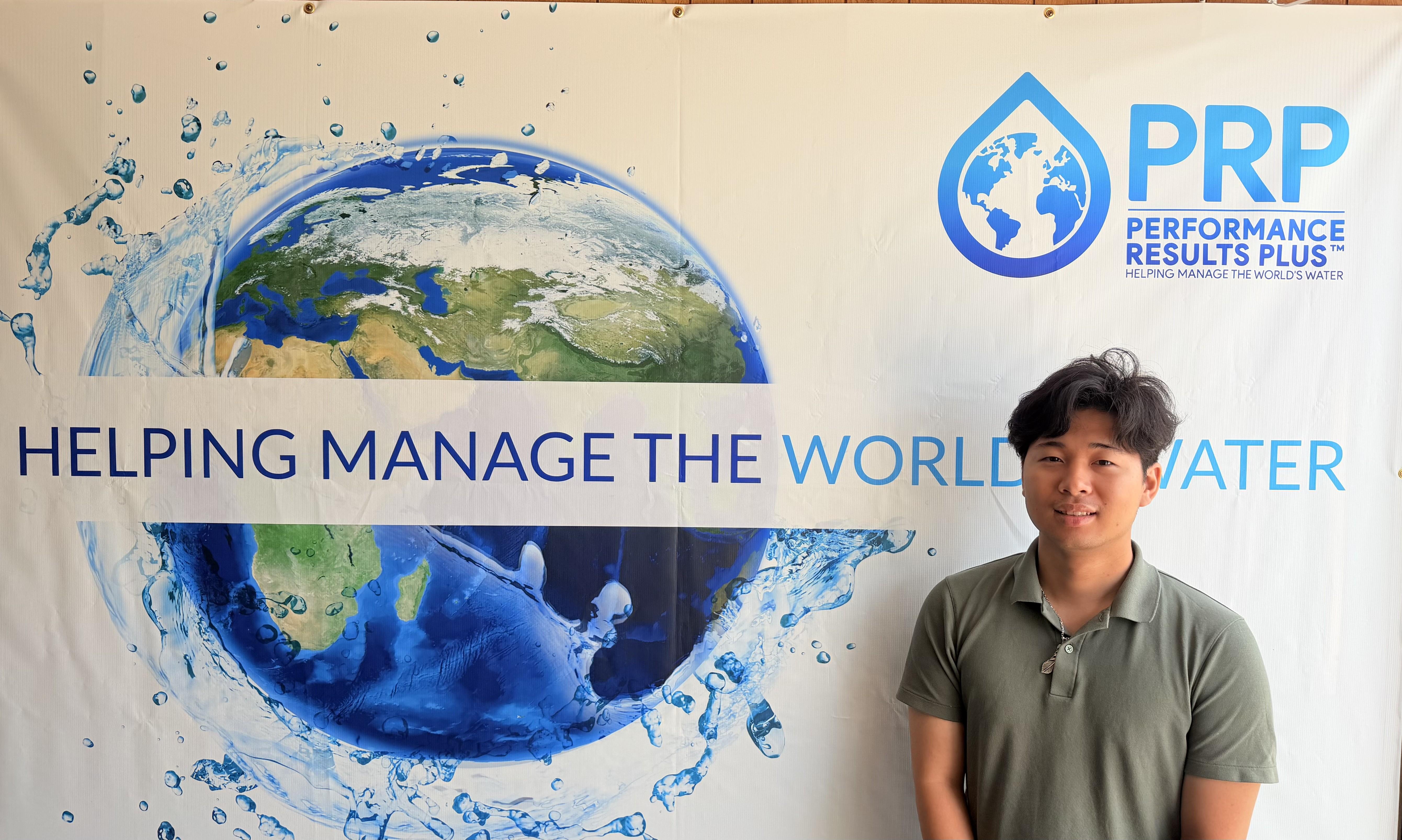 Shuto Urabe stands next to sign with PRP logo, image of world and phrase "Helping manage the world's water"