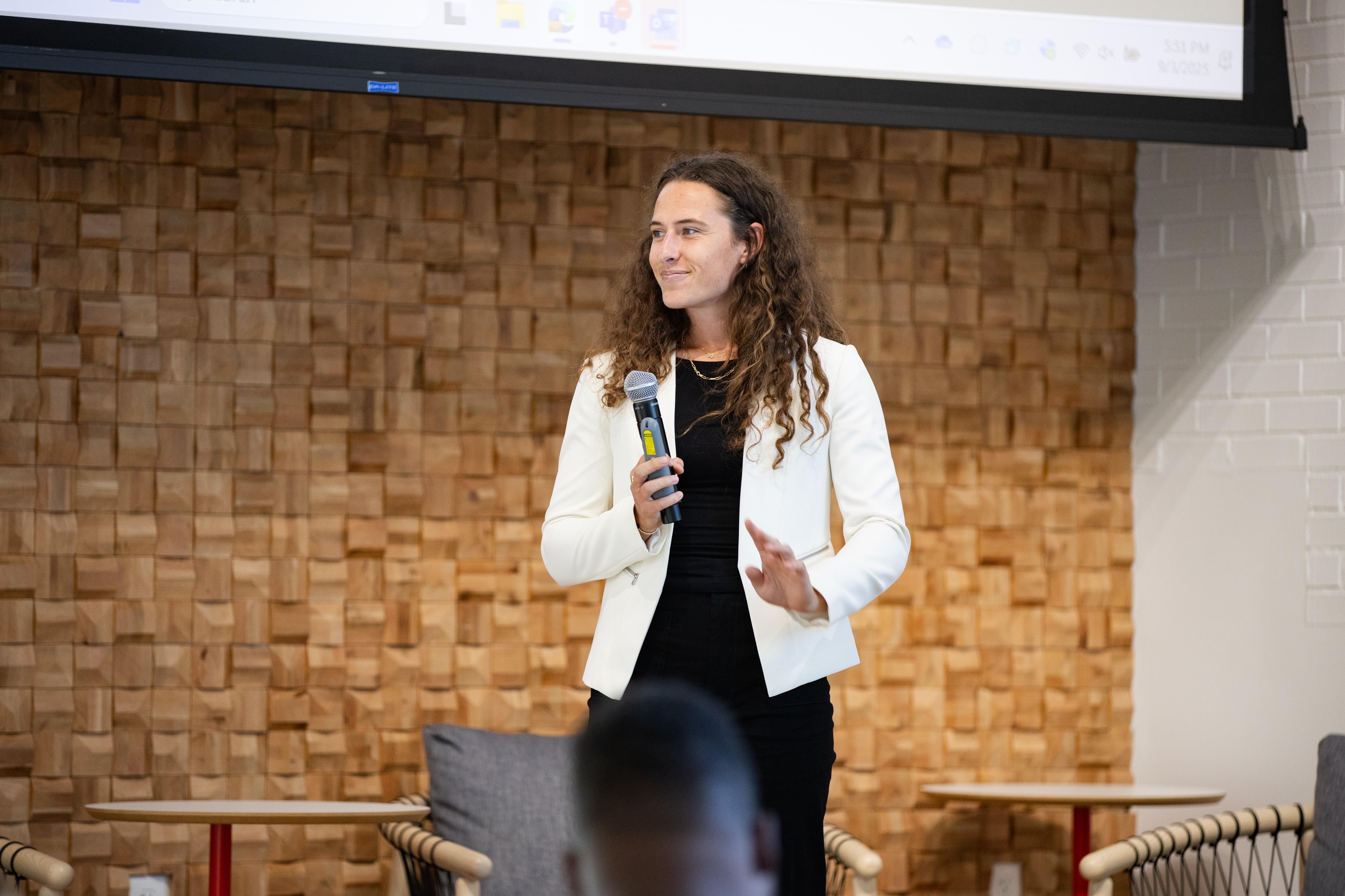 Amani McKavish-Kimball in white jacket holding microphone while giving presentation at Rockbridge