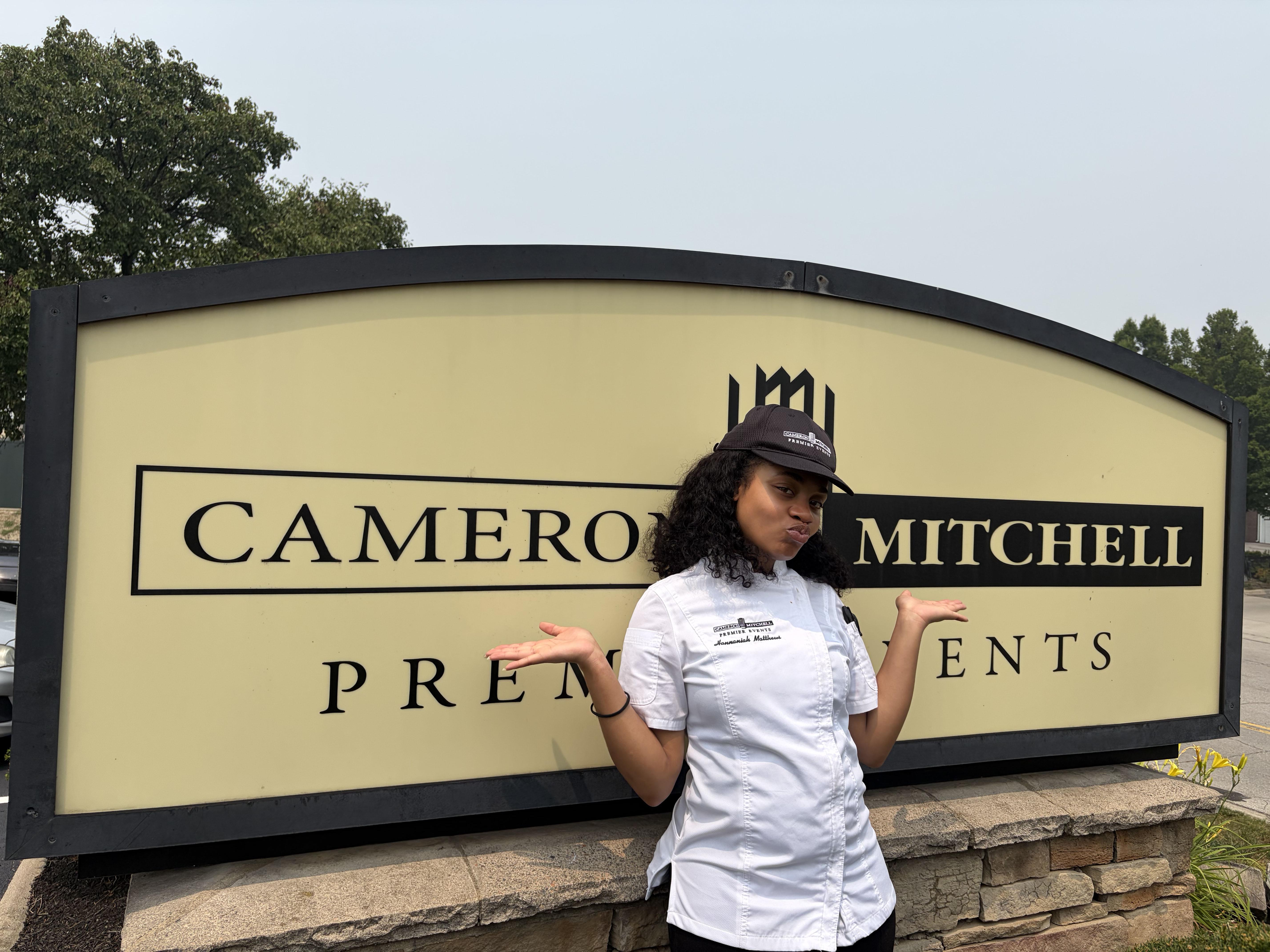 Woman in kitchen whites standing in front of a sign that says Cameron Mitchell Premiere events
