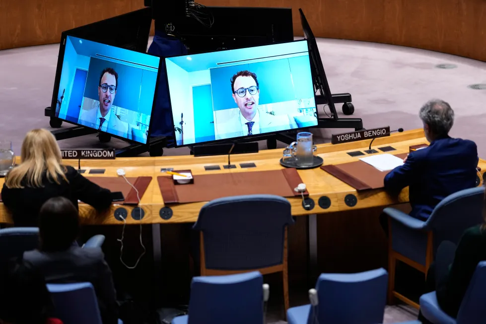Conference attendees face two large screens displaying a remote speaker.