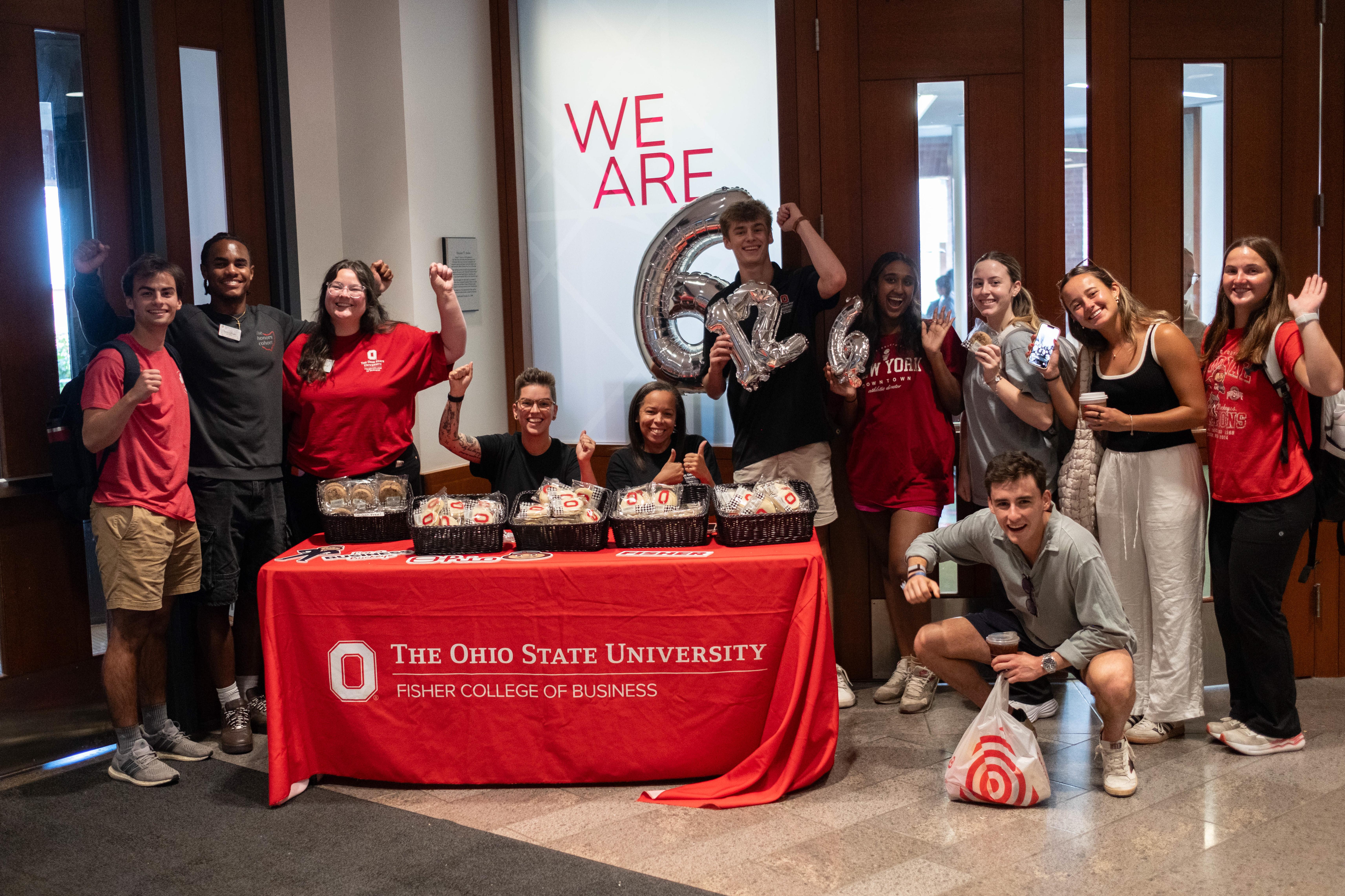 Group of people with thumbs up behind and beside table the "We are 6" behind them