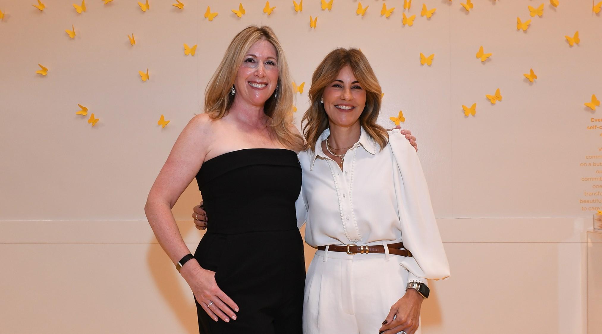 Rachel Friedman (EMBA '02) and Rhonda Hoffman (EMBA '13) pose together in front of a white wall filled with yellow butterfly post-it notes.