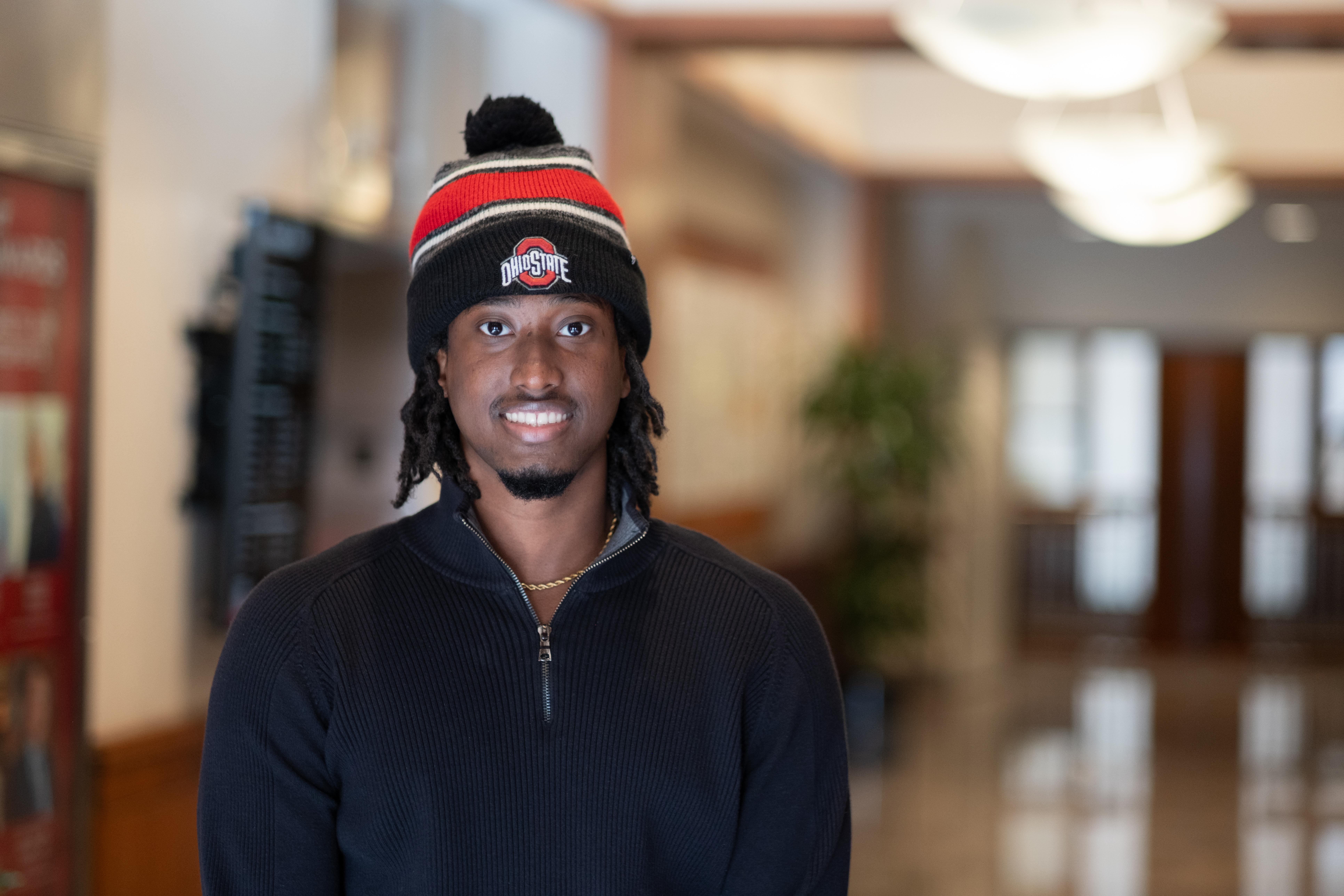 Lee in Ohio State hat and black jacket standing in hallway.