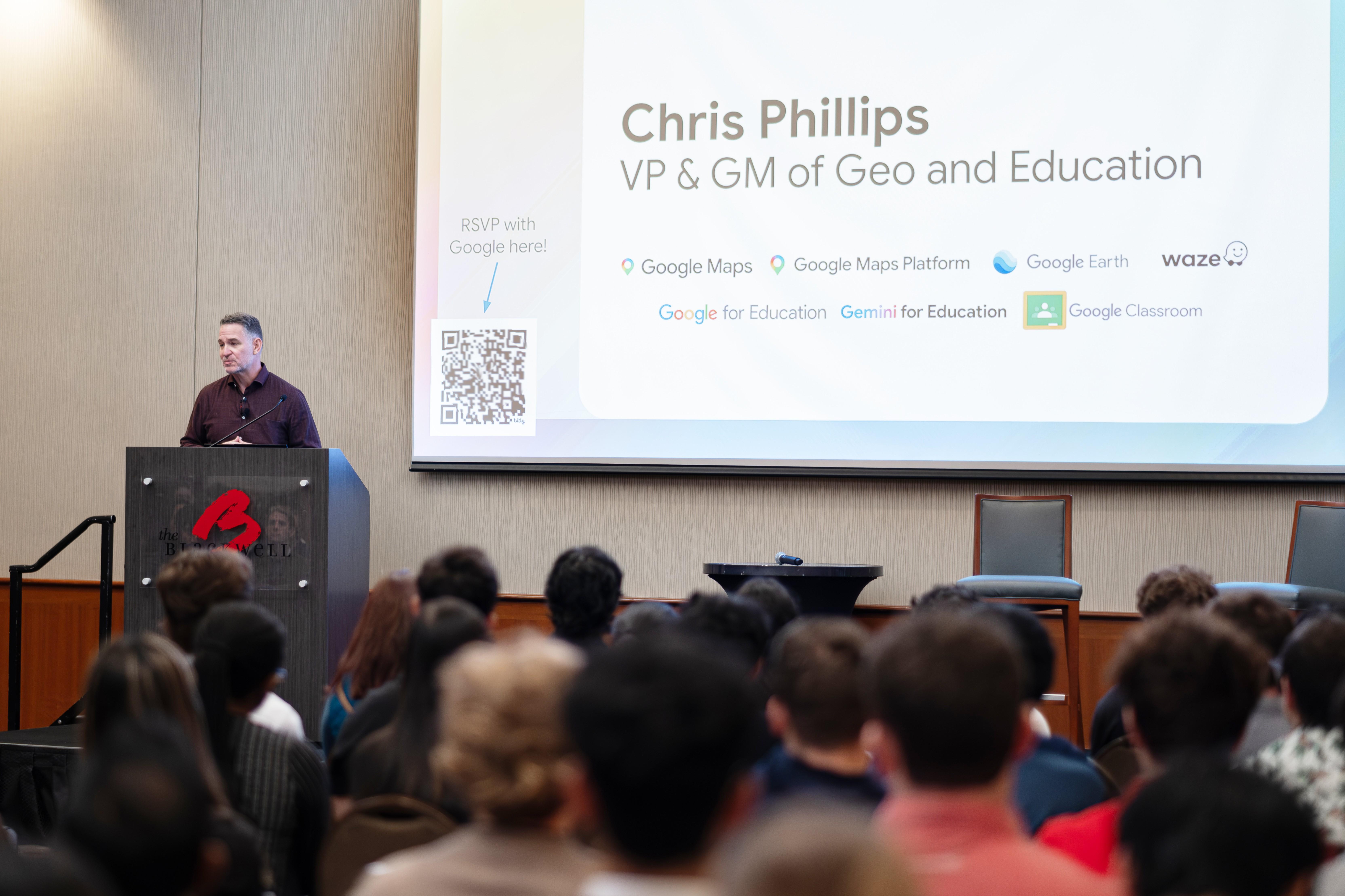 Chris Phillips standing behind podium with his name, title and Google products on screen behind him