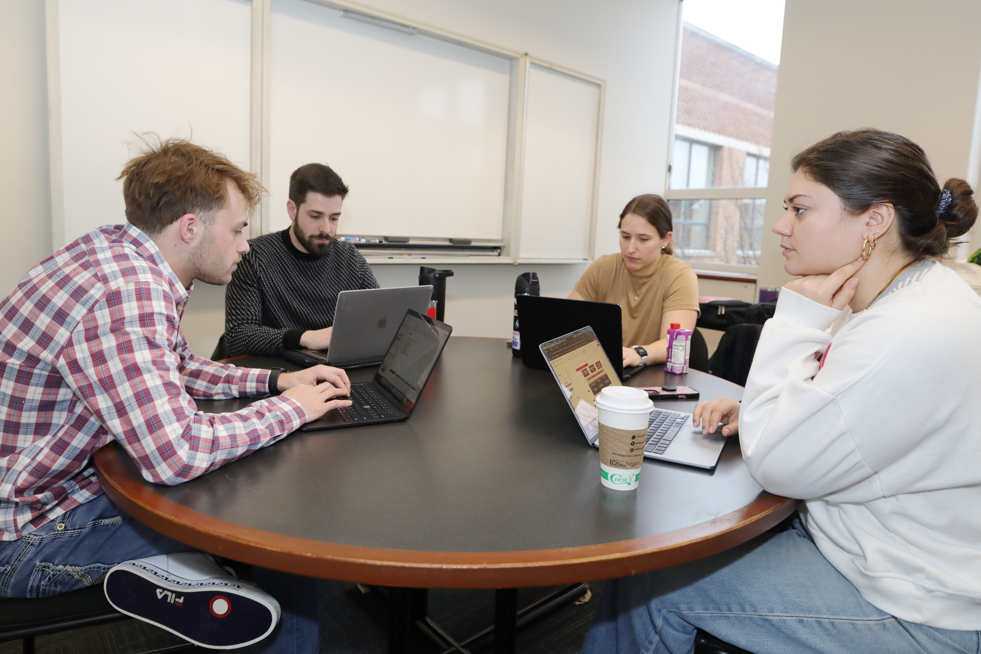 MBA students huddle around laptops working on a project in a conference room.