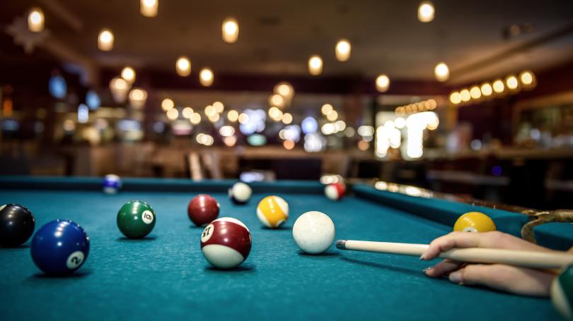 Hand on cue stick ready to strike the cue ball on a billiards tablel
