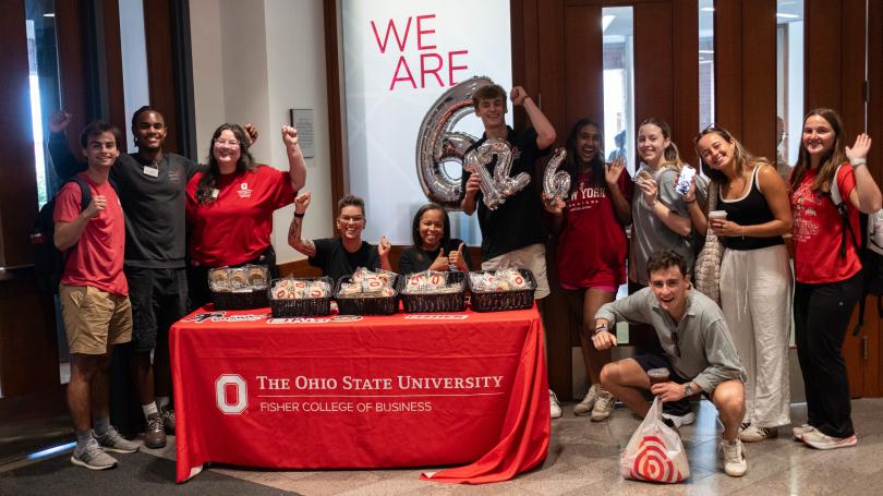 Group of people with thumbs up behind and beside table the "We are 6" behind them