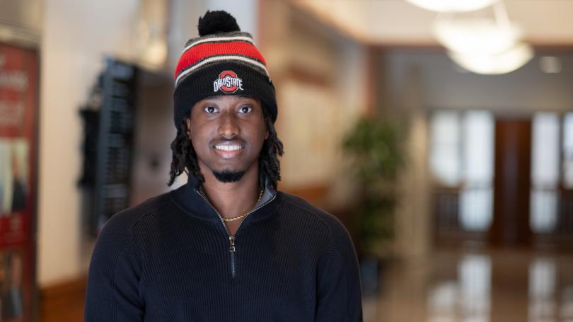 Lee in Ohio State hat and black jacket standing in hallway.