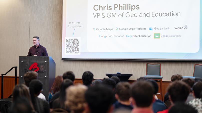 Chris Phillips standing behind podium with his name, title and Google products on screen behind him