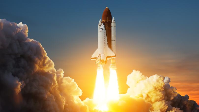 Space shuttle taking off with fire spewing out of jets creating clouds of smoke