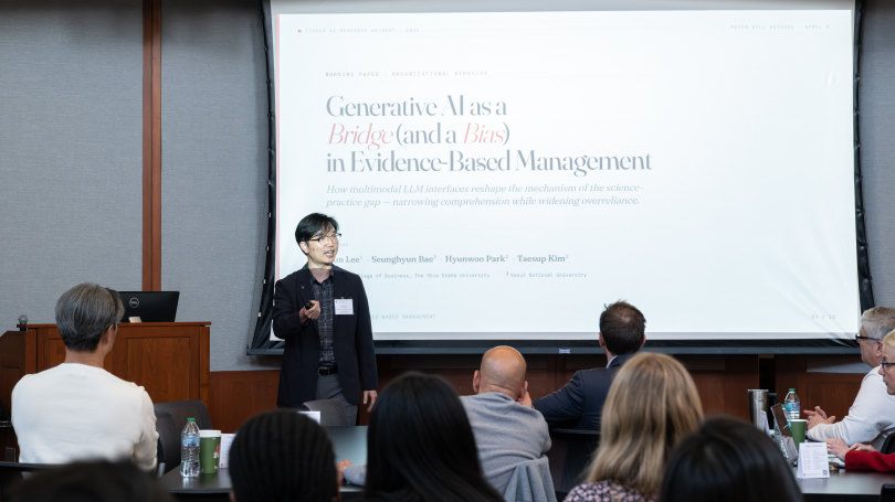 Hun Lee in suit in front of screen in small meeting room explaining his research