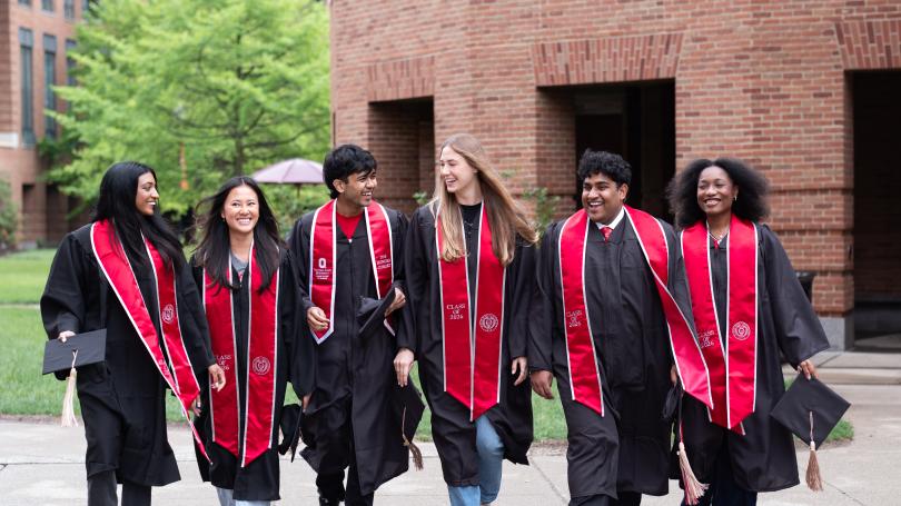 Group of students in graduation gowns walking across Fisher campus