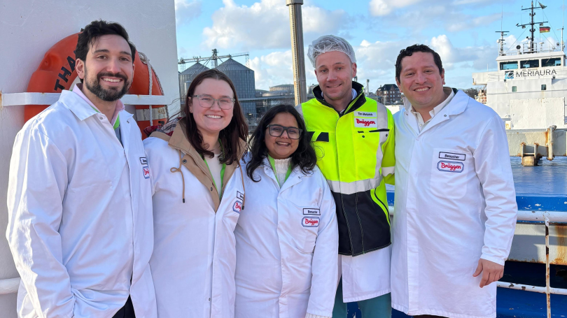 Group of MBA students in white lab coats posing on a ship deck during an industrial oat milling facility tour.