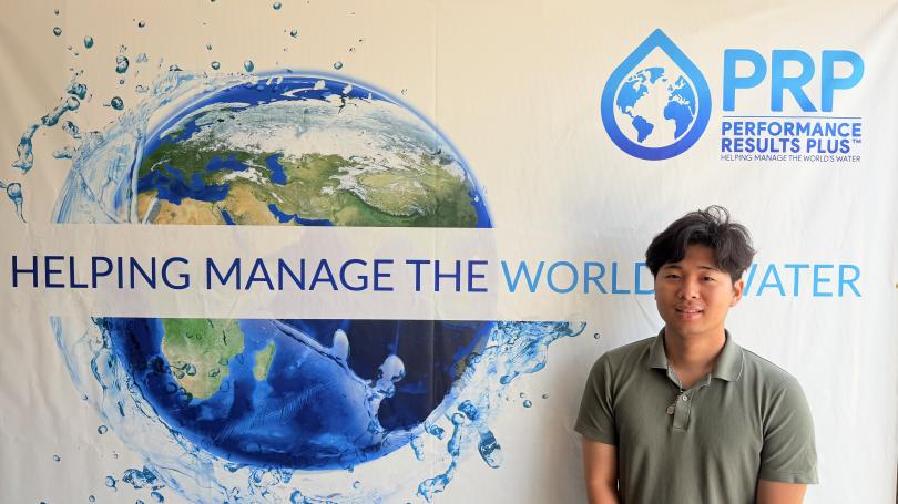 Shuto Urabe stands next to sign with PRP logo, image of world and phrase "Helping manage the world's water"