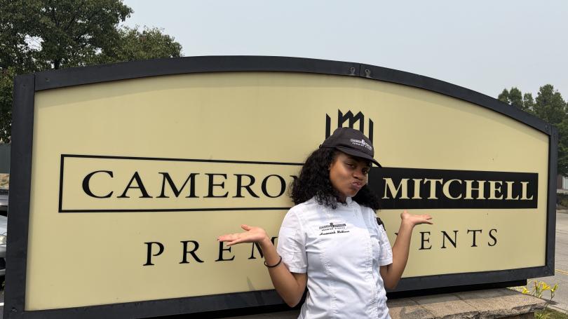 Woman in kitchen whites standing in front of a sign that says Cameron Mitchell Premiere events