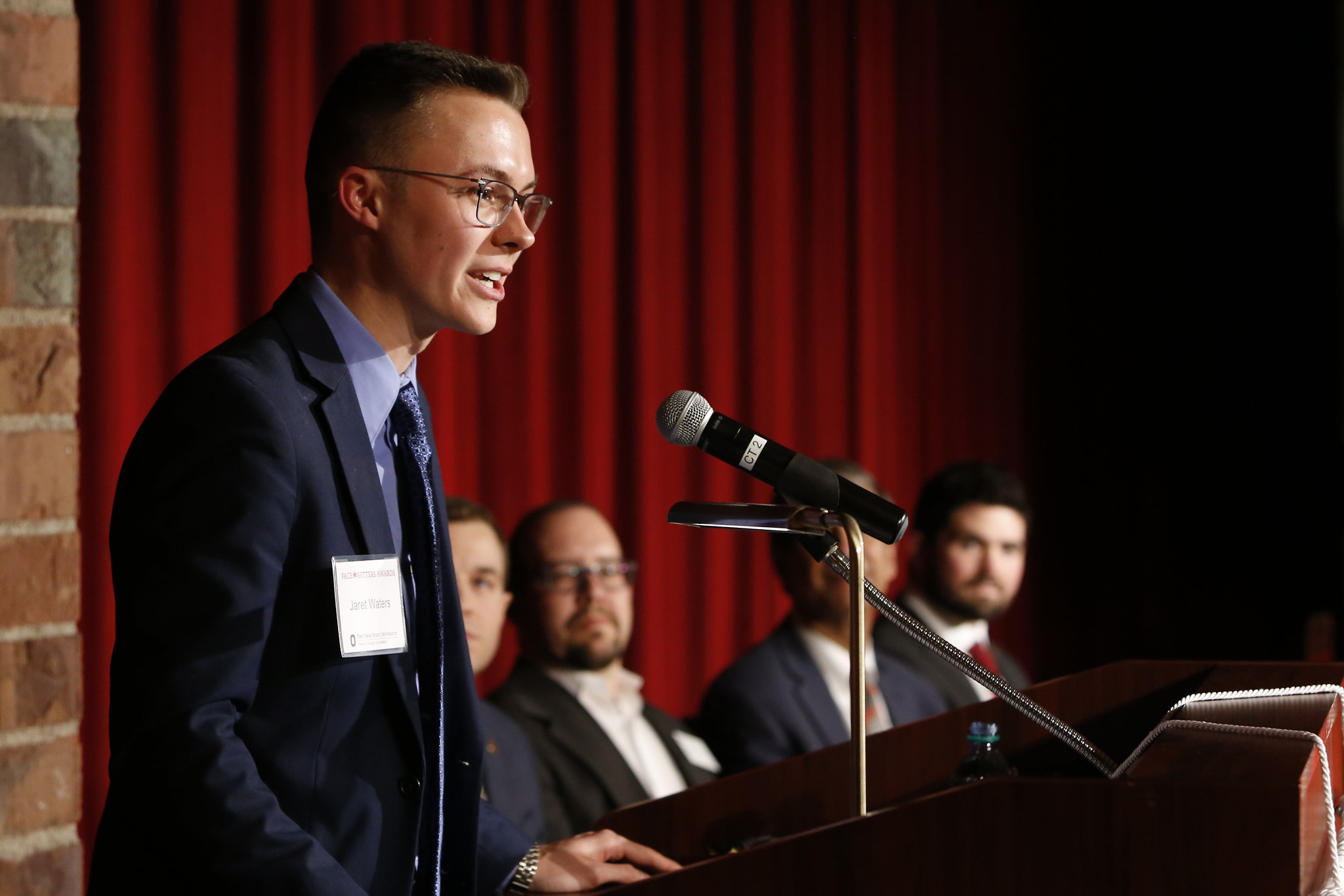student in a suit, speaking at a podium