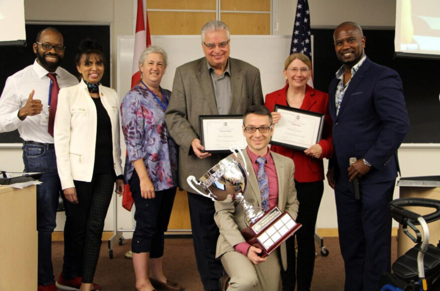 De gauche à droit : Rangée arrière - Leslie Benfield, directeur croissance des clubs D123; Iona Rodricks, directrice de la qualité des programmes D123; Kris Nelson, directrice de district D123; Mario Keriakedes, 2e place, Deborah Walker, 3e place, Roger Caesar, président du concours D123. Rangée avant – (celui avec le gros trophée) Alexandre Matte, 1re place. — Photo : Courtoisie