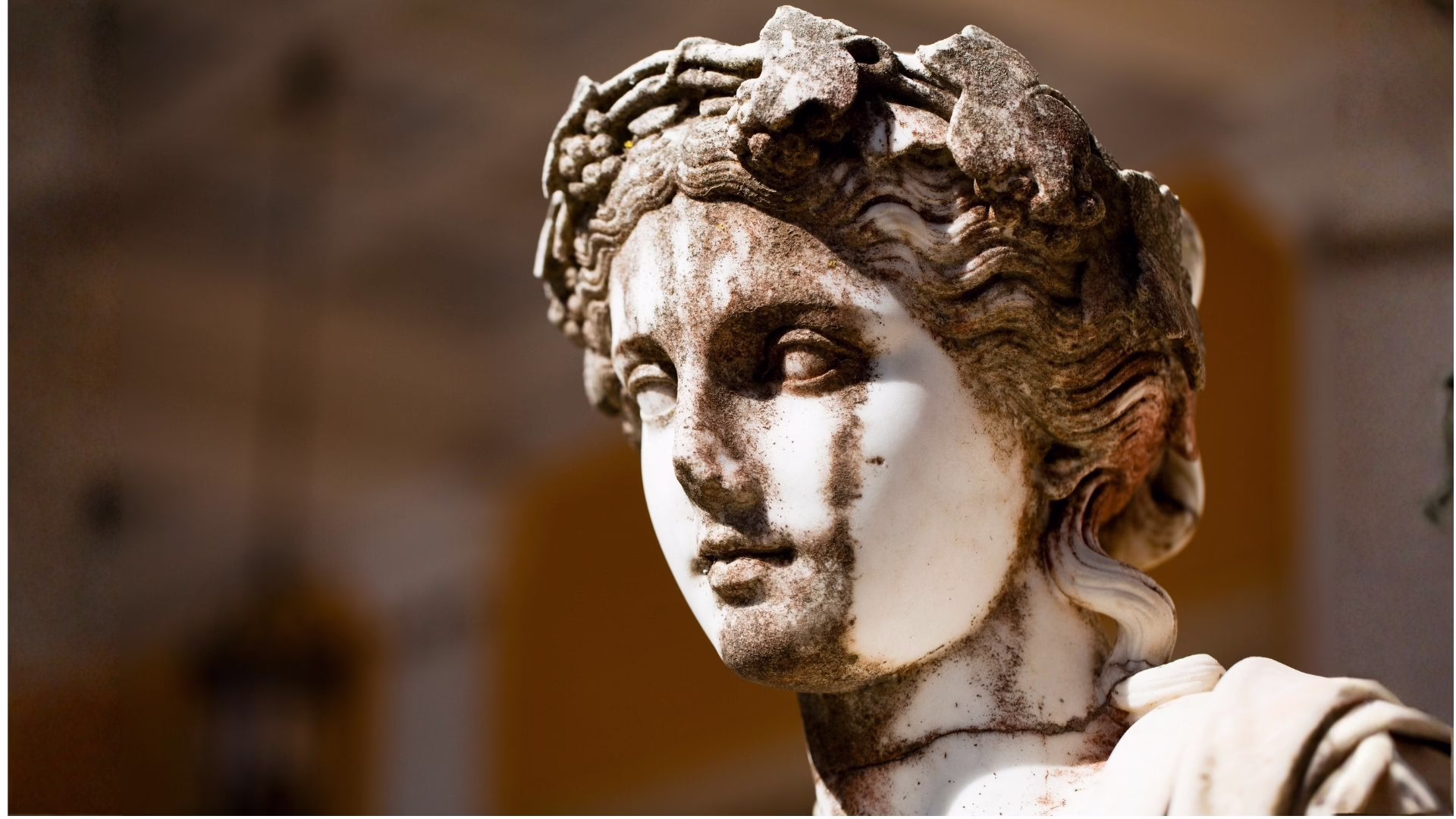 Close-up of a weathered marble statue bust with dark grime on the face and hair.