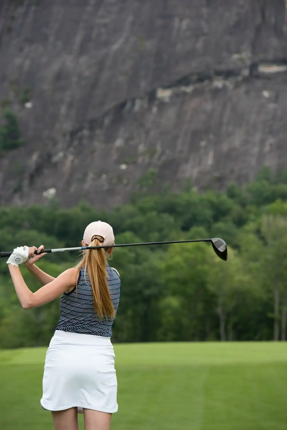 Woman swinging golf club with Rock Mountain in background