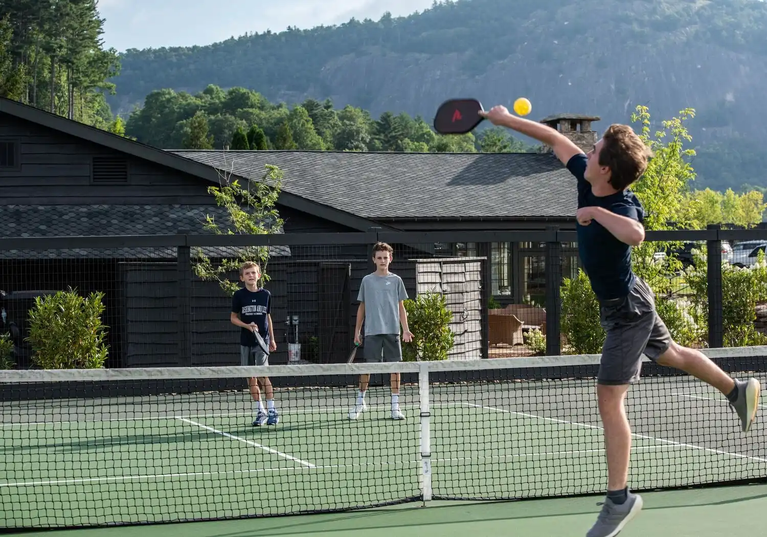 Three boys playing pickleball on a sunny day