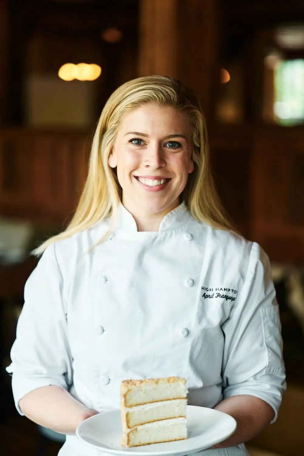 Pastry Chef April Franqueza smiles and holds a piece of coconut cake