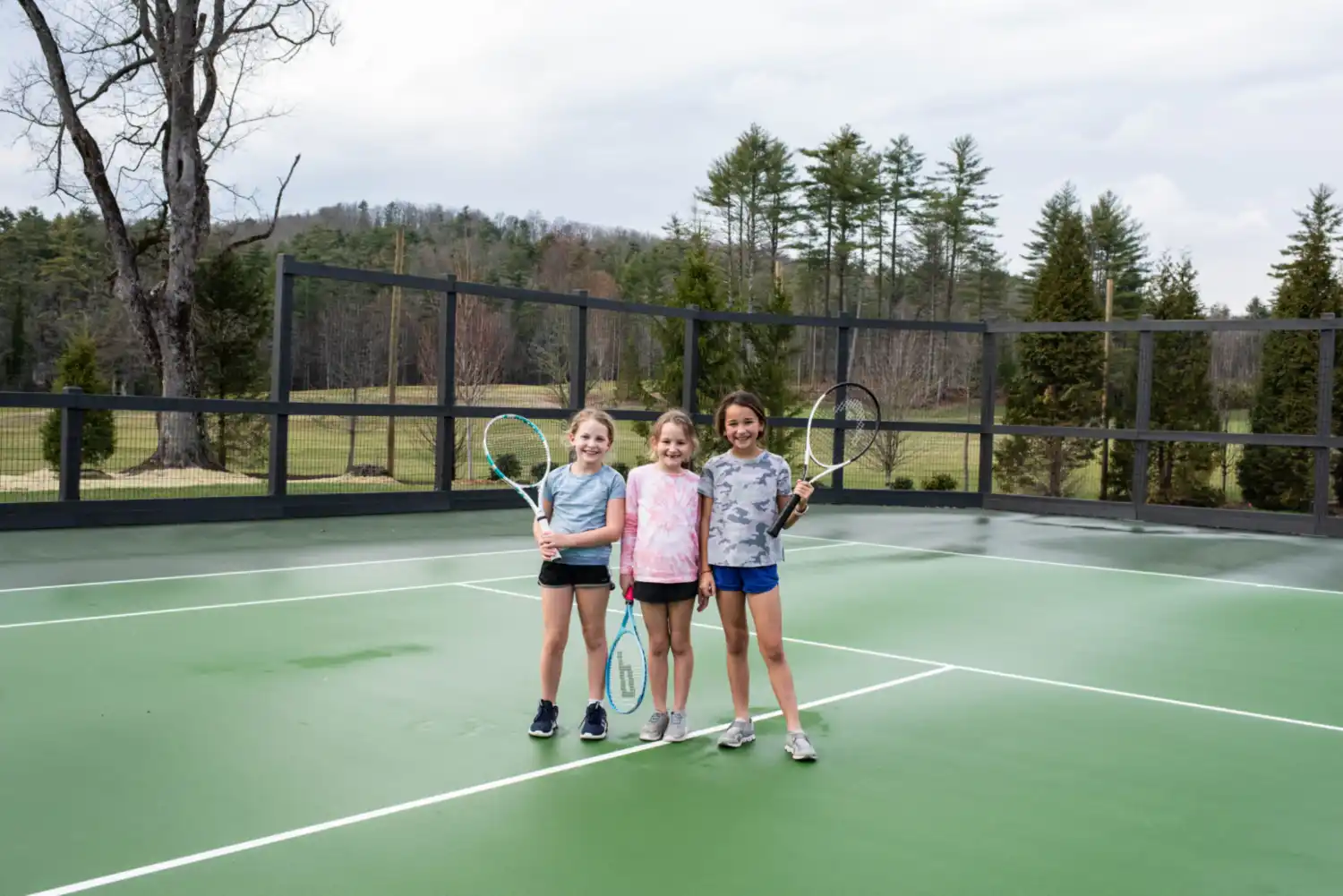 Three girls smiling on tennis court