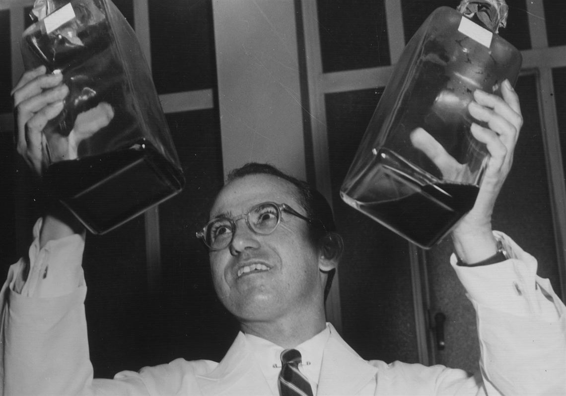 Dr. Jonas Salk holding a vial of the polio vaccine, speaking into a radio microphone.