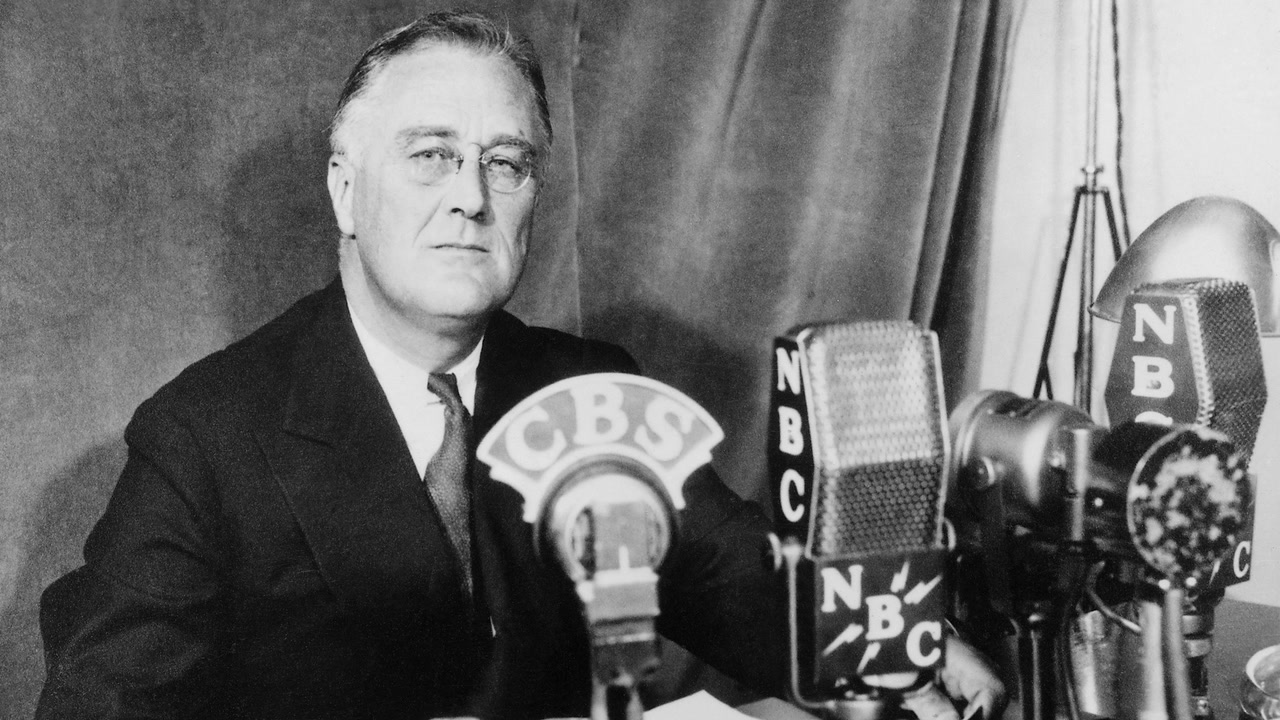 FDR seated at a desk giving his May 27, 1941 radio address, with a U.S. flag behind him.