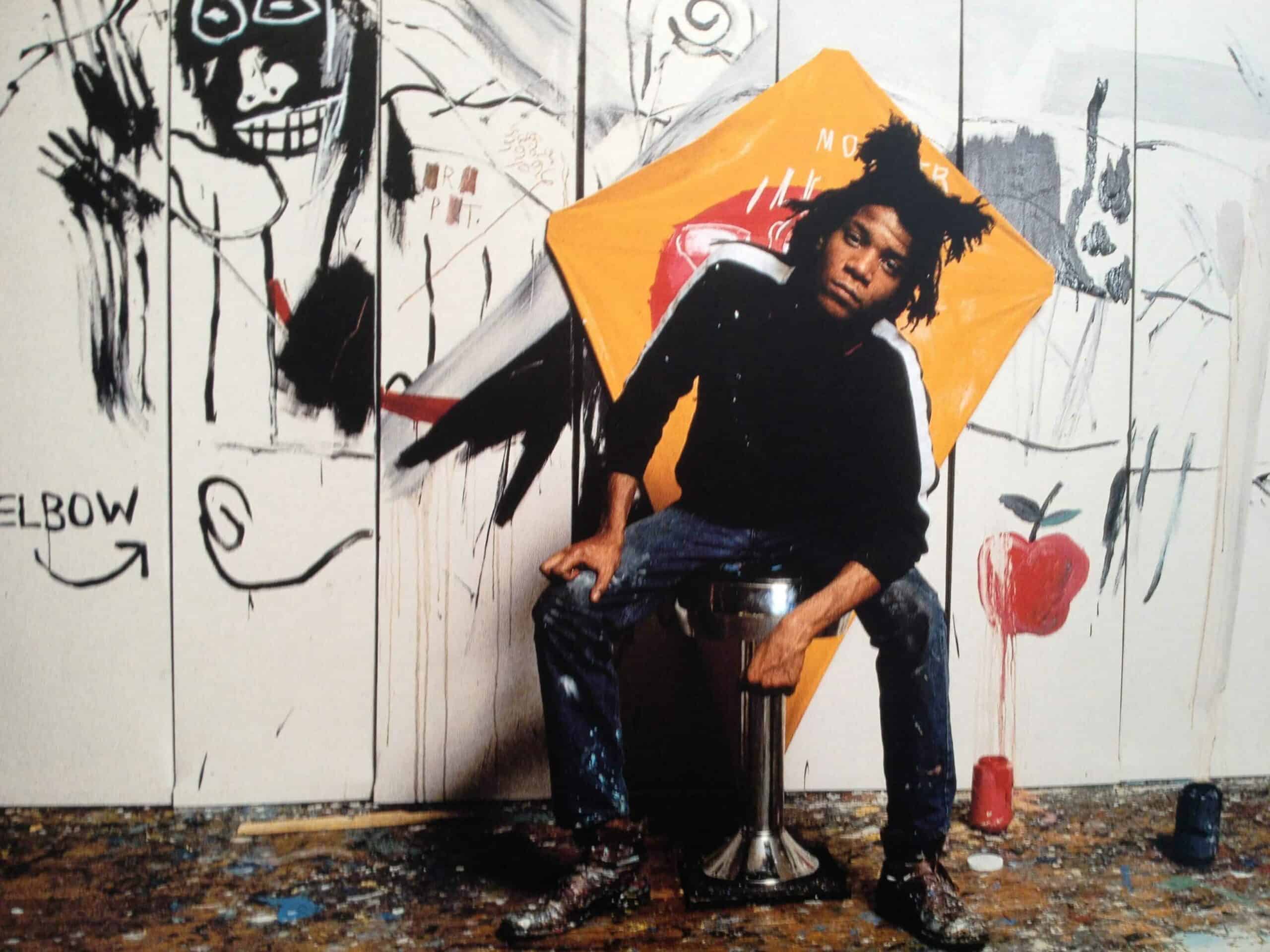 Jean-Michel Basquiat in his studio, wearing a paint-splattered shirt and gazing intently at a large canvas.