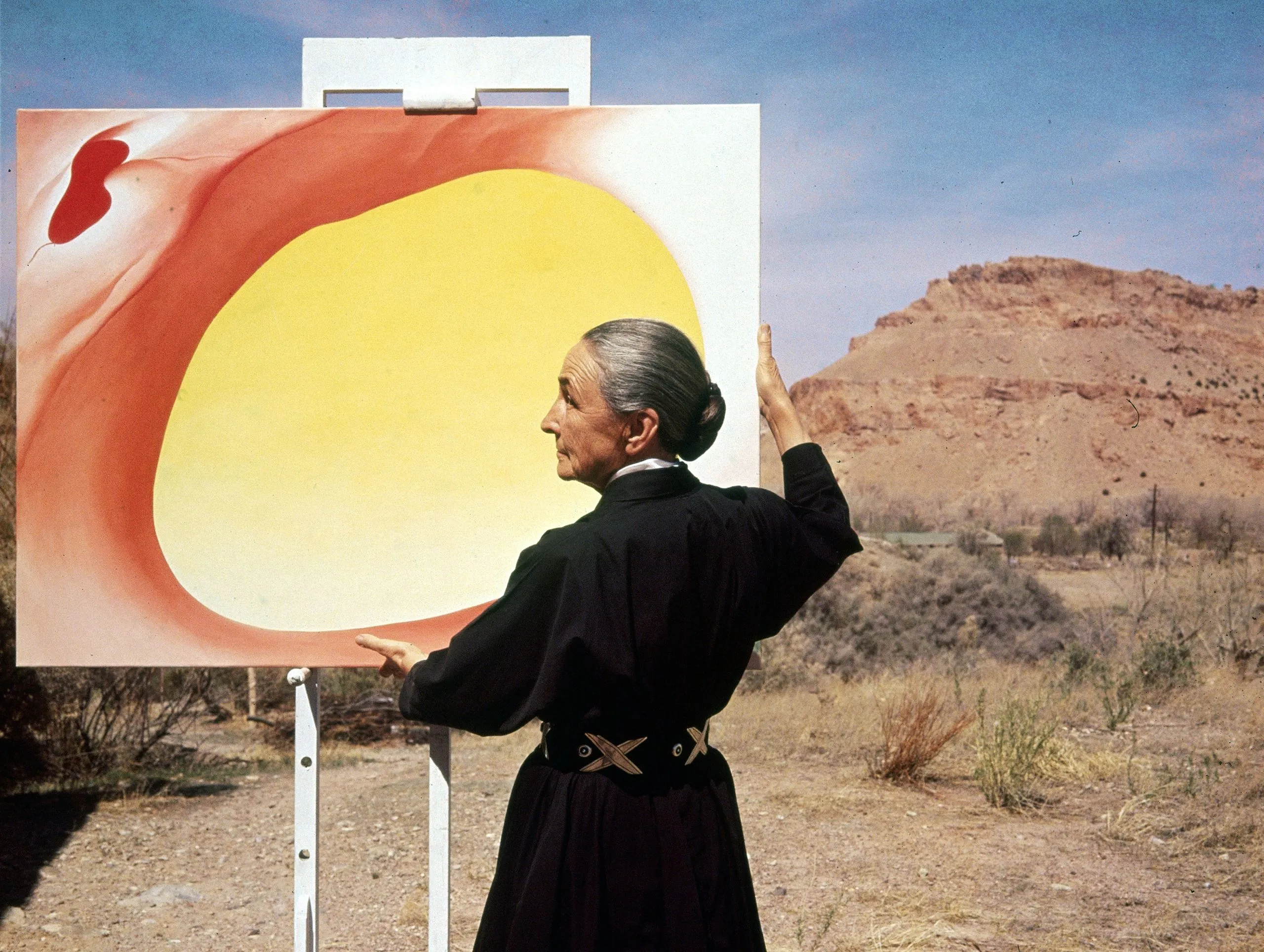 Georgia O’Keeffe standing in the New Mexico desert, wearing black and looking strong and independent against the vast horizon.