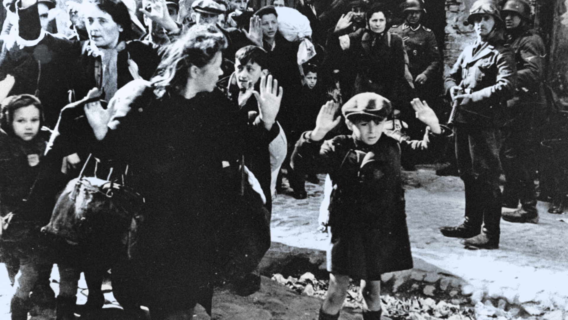 Black-and-white photo of Jewish families with suitcases being marched by Nazi soldiers through the streets of Warsaw.