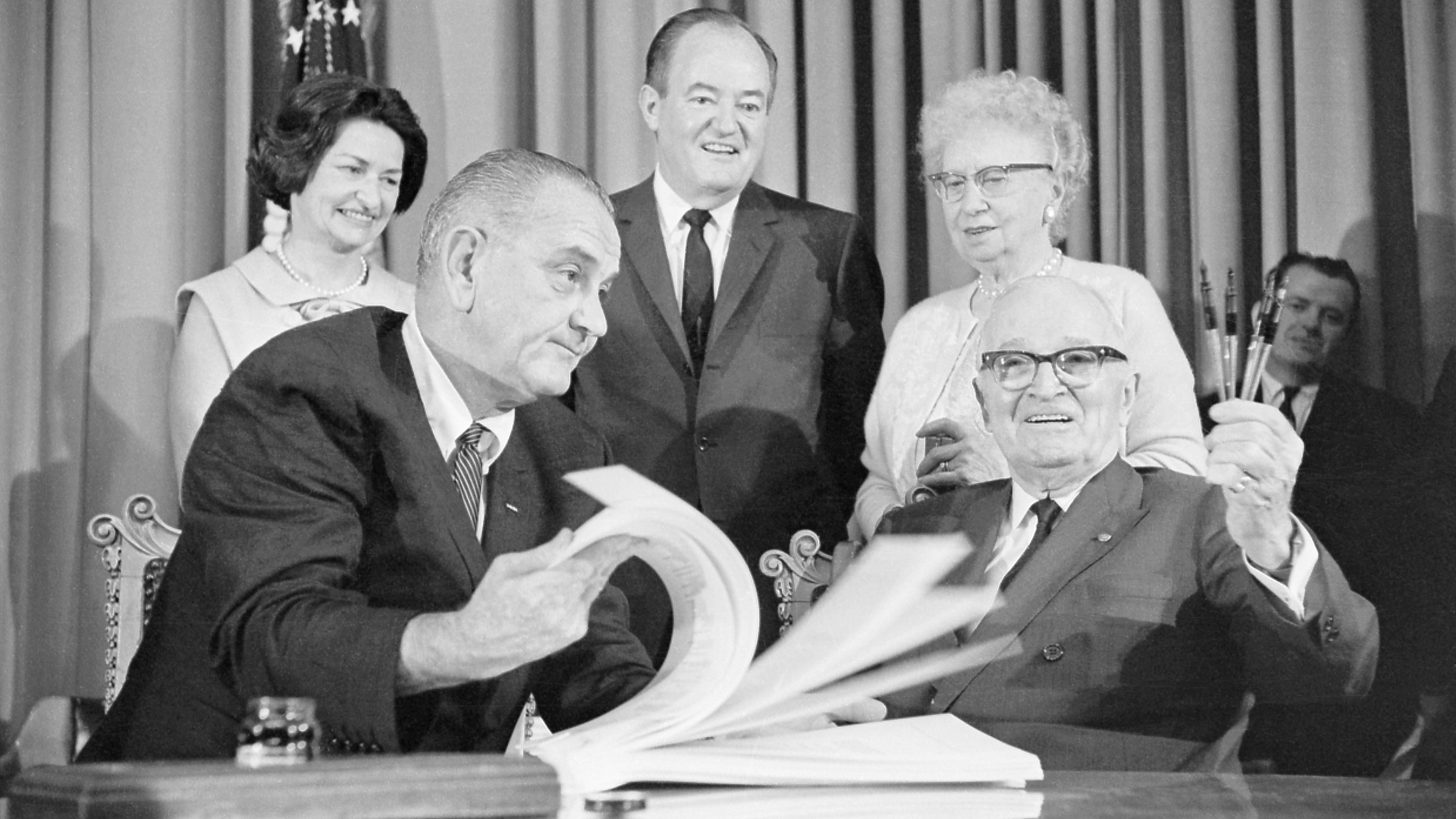 President Lyndon B. Johnson signs the Medicare and Medicaid Act next to former President Harry Truman.