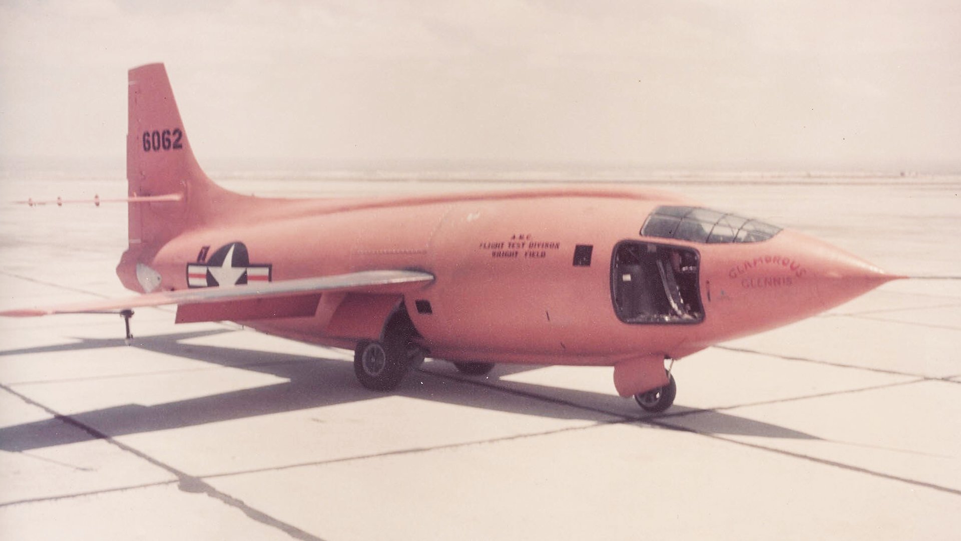 The orange Bell X-1 rocket plane, Glamorous Glennis, in flight over the desert.