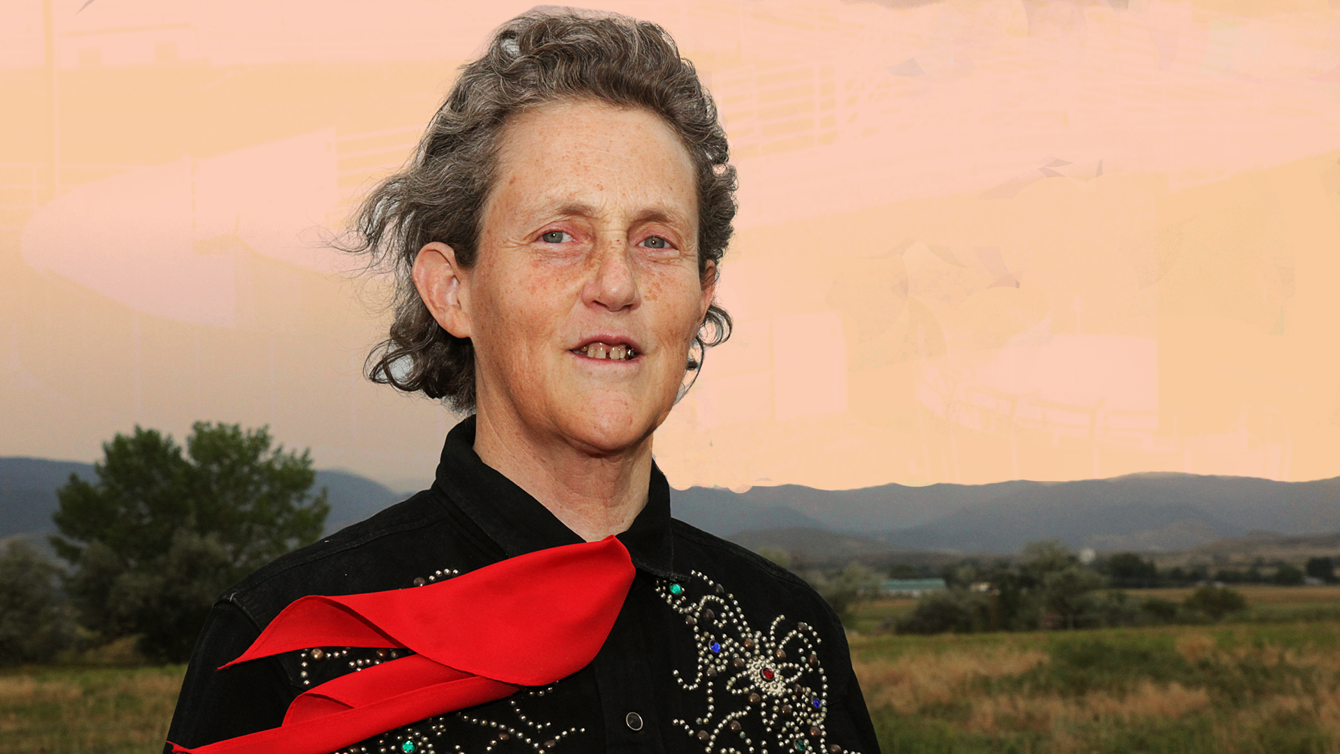 Temple Grandin standing confidently in front of a barn, wearing her signature western shirt and bolo tie.