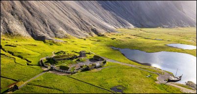 Aerial view of a green valley a Viking Village surrounded by towering Vestrahorn mountains in Stokksnes in Iceland. A serene atmosphere with lakes and historic structures historical landscape