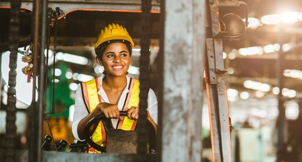 Employee driving fork lift in warehouse while wearing safety helmet