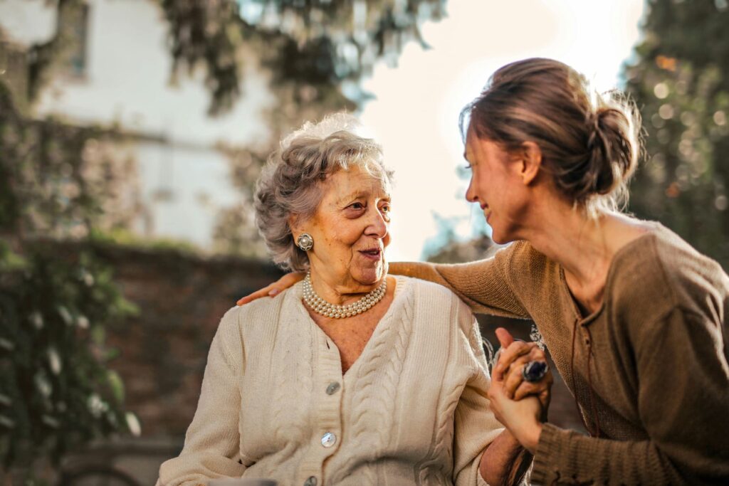 An old woman smiling at a younger woman as they hold hands and sit together.