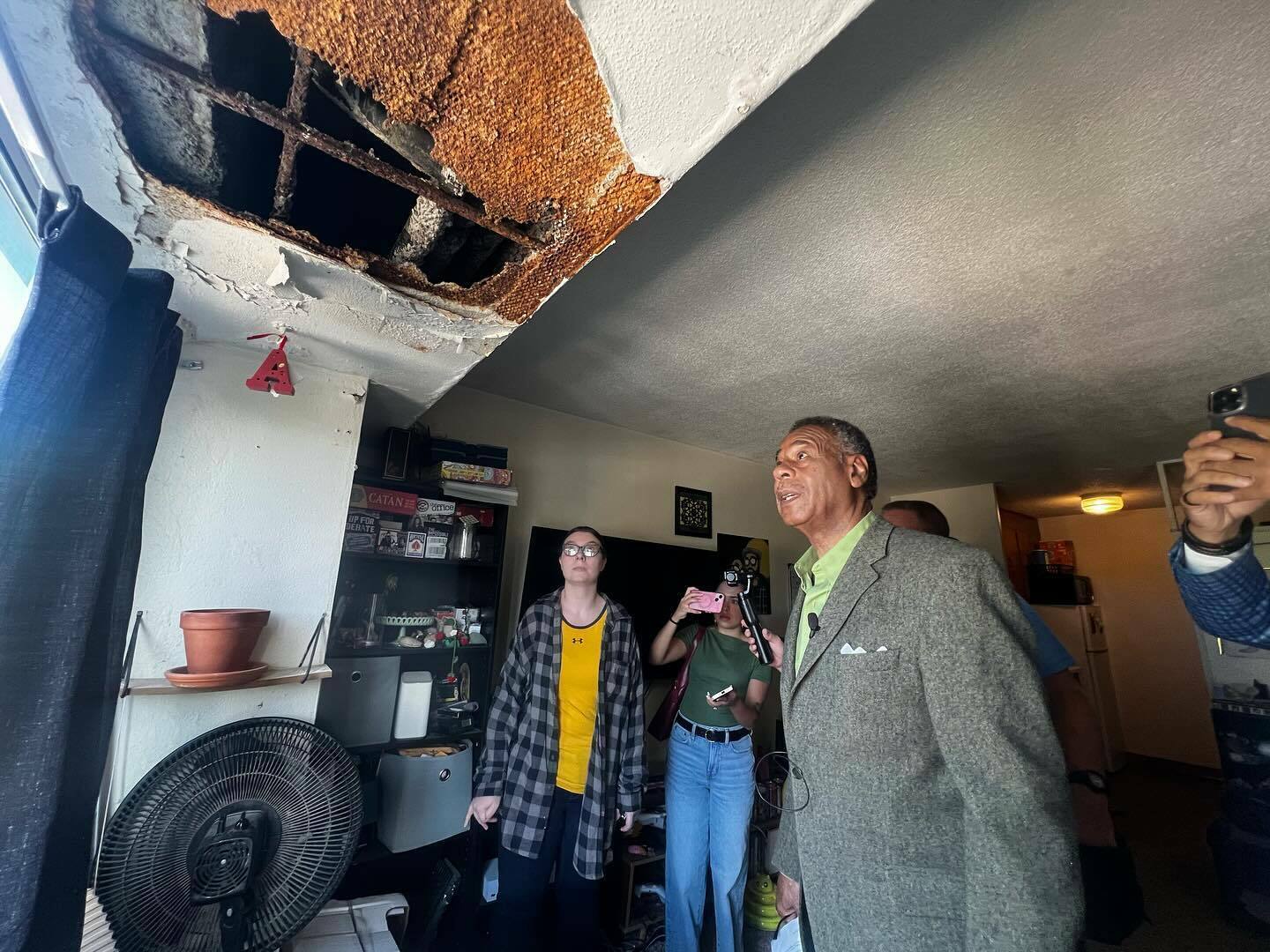 three people stand looking up at a large hole in a ceiling.