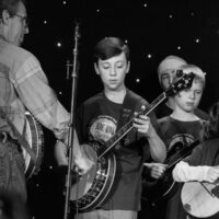 Ira Gitlin holds mic for banjo solo in the Kids Academy band at Joe Val (2/19/17) - photo © Tara Linhardt