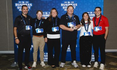 Six Richmond Flying Squirrels staff members pose in front of a 2026 MiLB Business Summit backdrop in Louisville, with one holding the Organization of the Year trophy.