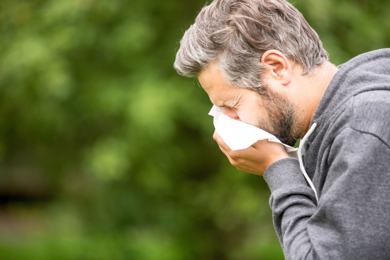 Man sneezing outside into a tissue because of allergies