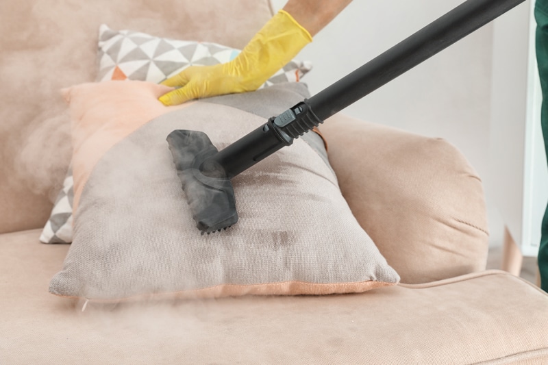 Person with yellow gloves steam cleans a pillow on a chair