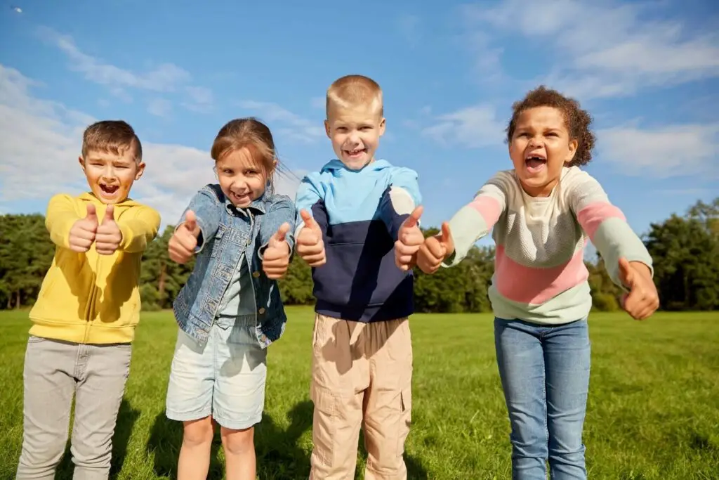 Preschool kids smiling at the camera while giving a double thumbs up.