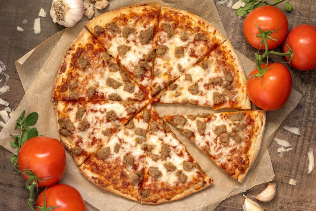 Top down photo of a baked Italian Sausage pizza. The pizza is on brown parchment paper with ingredients scattered all around.