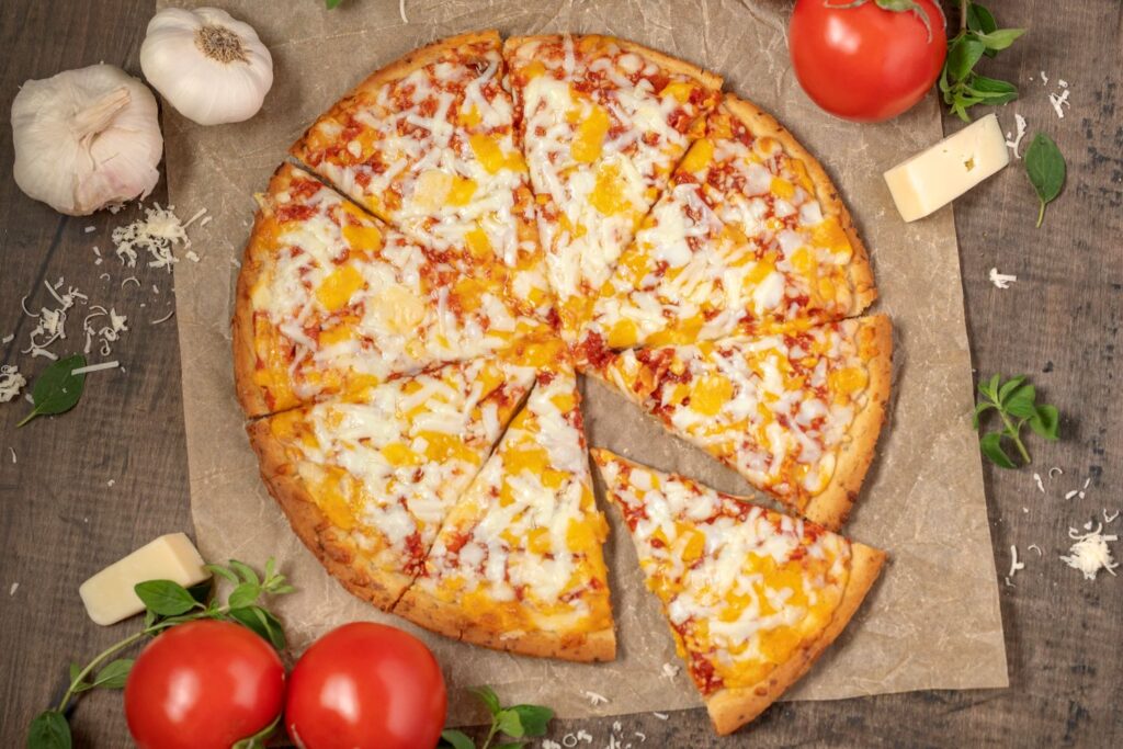 Top down photo of a baked 3 Cheese gluten free pizza. The pizza is on brown parchment paper with ingredients scattered all around.