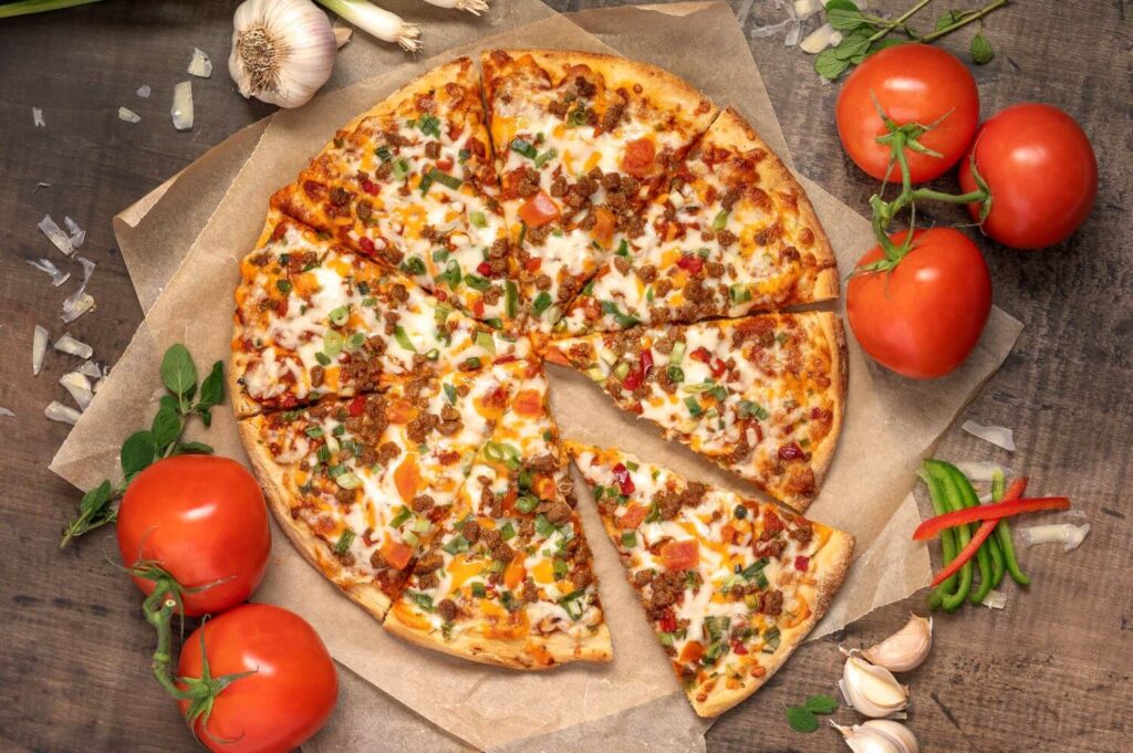 Top down photo of a baked Beef Taco pizza. The pizza is on brown parchment paper with ingredients scattered all around.