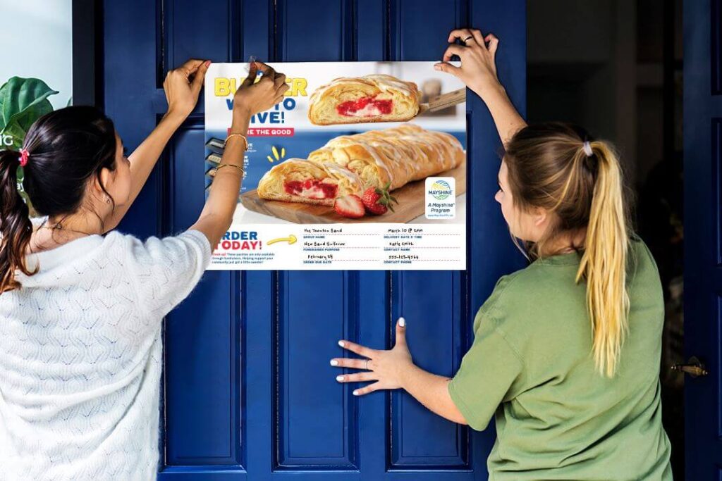 Two high school girls putting up a poster for their Butter Braid Pastry Fundraiser.