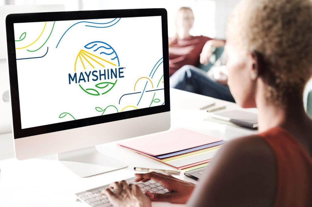 Woman on her computer. On the screen is a large Mayshine logo.
