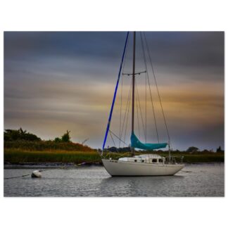 A white sailboat with blue rigging floats on calm water at sunset, surrounded by lush green reeds. The sky is a blend of orange and blue hues.